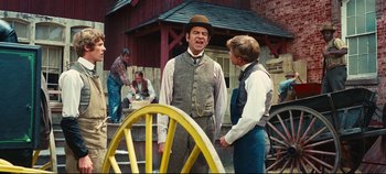 Movie still from “Hello, Dolly!” (1969), directed by Gene Kelly – Two men in old - fashioned clothing standing next to a wagon wheel; Medium shot, Over the shoulder angle