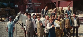 Movie still from “Hello, Dolly!” (1969), directed by Gene Kelly – A group of men standing next to each other in front of a building; Wide shot, Low angle