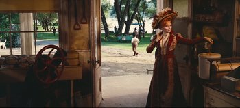 Movie still from “Hello, Dolly!” (1969), directed by Gene Kelly – A woman in a red and brown dress talking on a phone; Wide shot, Over the shoulder angle