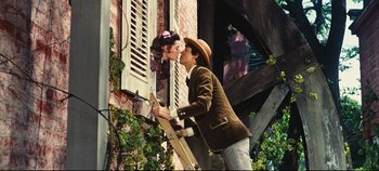 Movie still from “Hello, Dolly!” (1969), directed by Gene Kelly – A man and a woman kissing in front of an open window; Medium shot, Low angle