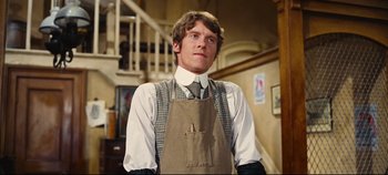 Movie still from “Hello, Dolly!” (1969), directed by Gene Kelly – A man wearing an apron standing in front of a staircase; Medium shot, Low angle