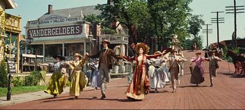 Movie still from “Hello, Dolly!” (1969), directed by Gene Kelly – A group of people dressed in period clothing walking down a street; Wide shot, Low angle