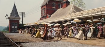 Movie still from “Hello, Dolly!” (1969), directed by Gene Kelly – A group of people walking down a street holding parasols; Extreme Wide shot, High angle