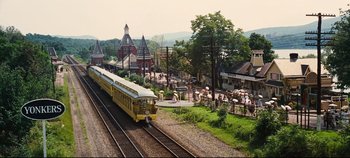 Movie still from “Hello, Dolly!” (1969), directed by Gene Kelly – A yellow train traveling down train tracks next to a park; Extreme Wide shot, High angle