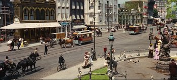 Movie still from “Hello, Dolly!” (1969), directed by Gene Kelly – A street scene with horse drawn carriages and people on bicycles; Extreme Wide shot, High angle