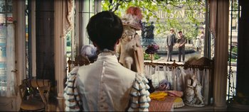 Movie still from “Hello, Dolly!” (1969), directed by Gene Kelly – A woman standing in front of a statue of a person; Wide shot, Over the shoulder angle