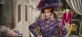 Movie still from “Hello, Dolly!” (1969), directed by Gene Kelly – A woman wearing a purple dress and a purple hat; Medium shot, Over the shoulder angle