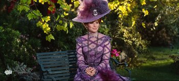Movie still from “Hello, Dolly!” (1969), directed by Gene Kelly – A woman in a purple dress and a hat sitting on a park bench; Medium shot, Over the shoulder angle