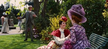 Movie still from “Hello, Dolly!” (1969), directed by Gene Kelly – Two women and a man are sitting in the grass; Wide shot, Over the shoulder angle