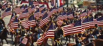 Movie still from “Hello, Dolly!” (1969), directed by Gene Kelly – A group of people on horses holding american flags; Wide shot, High angle