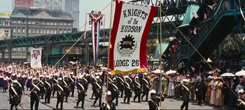 Movie still from “Hello, Dolly!” (1969), directed by Gene Kelly – A large group of people marching down a street; Wide shot, Low angle
