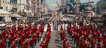 Movie still from “Hello, Dolly!” (1969), directed by Gene Kelly – A parade is going down a street with a lot of people marching; Extreme Wide shot, High angle