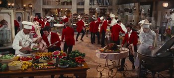 Movie still from “Hello, Dolly!” (1969), directed by Gene Kelly – A group of people dressed in red jackets in a kitchen; Wide shot, High angle
