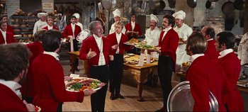 Movie still from “Hello, Dolly!” (1969), directed by Gene Kelly – A group of men standing in a kitchen holding trays of food; Wide shot, High angle