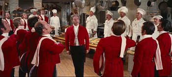 Movie still from “Hello, Dolly!” (1969), directed by Gene Kelly – A group of people dressed in red and white in a kitchen; Medium shot, Over the shoulder angle