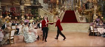 Movie still from “Hello, Dolly!” (1969), directed by Gene Kelly – Two men in red jackets holding a tray in a ballroom; Wide shot, High angle