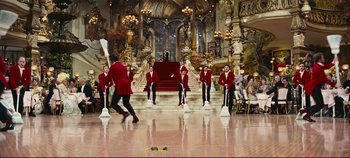 Movie still from “Hello, Dolly!” (1969), directed by Gene Kelly – A group of men in red jackets standing in front of a staircase; Extreme Wide shot, High angle