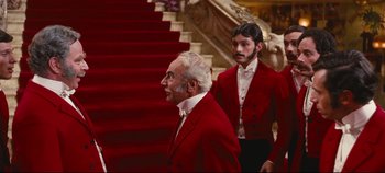 Movie still from “Hello, Dolly!” (1969), directed by Gene Kelly – A man in a red suit standing next to another man in a red suit; Medium shot, Over the shoulder angle