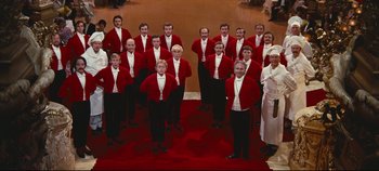 Movie still from “Hello, Dolly!” (1969), directed by Gene Kelly – A group of men standing next to each other on a red carpet; Wide shot, High angle