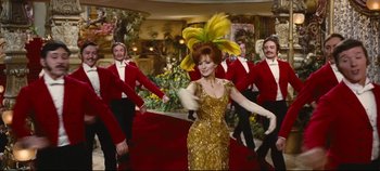 Movie still from “Hello, Dolly!” (1969), directed by Gene Kelly – A woman in a gold dress and a yellow feather hat; Wide shot, Low angle