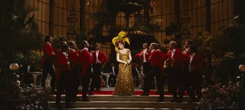 Movie still from “Hello, Dolly!” (1969), directed by Gene Kelly – A woman in a gold dress surrounded by men in red jackets; Wide shot, Low angle