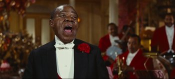 Movie still from “Hello, Dolly!” (1969), directed by Gene Kelly – An older man in a black suit and a red flower in his lapel; Medium shot, Low angle