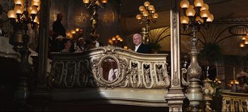 Movie still from “Hello, Dolly!” (1969), directed by Gene Kelly – An older man standing on a balcony in front of people; Wide shot, Low angle