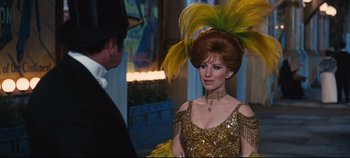 Movie still from “Hello, Dolly!” (1969), directed by Gene Kelly – A woman in a gold dress with a yellow feathered headdress; Medium shot, Over the shoulder angle