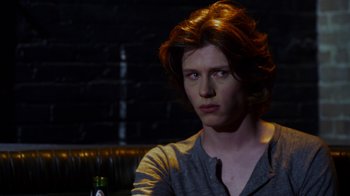 Movie still from “Hellraiser: Revelations” (2011), directed by Víctor Garcia – A man with long red hair sitting at a table with a bottle; Close Up shot, Over the shoulder angle