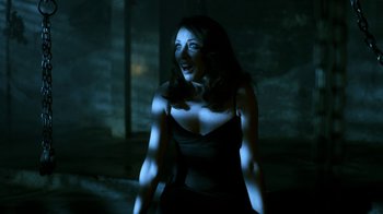 Movie still from “Hellraiser: Revelations” (2011), directed by Víctor Garcia – A woman in a black top is standing in a dark room; Medium shot, Low angle