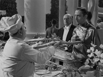 Movie still from “Hellzapoppin'” (1941), directed by H.C. Potter – A man in a chef's hat is serving a plate of food to another man in a tuxedo; Medium shot, Over the shoulder angle