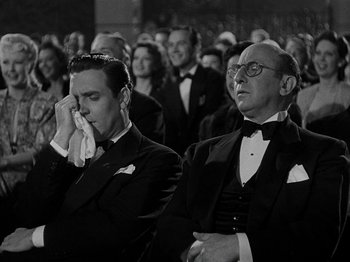 Movie still from “Hellzapoppin'” (1941), directed by H.C. Potter – Two men in tuxedos are sitting in a crowd of people; Medium shot, Low angle