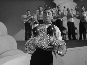Movie still from “Hellzapoppin'” (1941), directed by H.C. Potter – A man in a black and white photo holding balloons in front of a group of people; Medium shot, Low angle