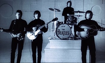 Movie still from “Help!” (1965), directed by Richard Lester – A group of people that are standing up in a room; Wide shot, Low angle