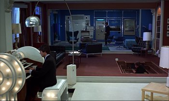 Movie still from “Help!” (1965), directed by Richard Lester – A man sitting at a piano in a room with furniture; Wide shot, High angle