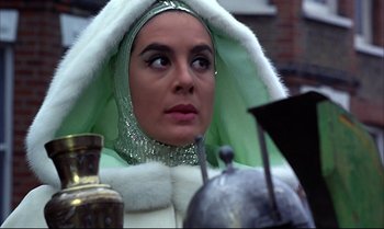 Movie still from “Help!” (1965), directed by Richard Lester – A woman in a green and white outfit with a hood on; Close Up shot, Low angle