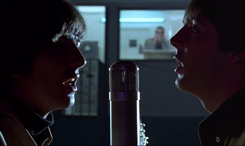 Movie still from “Help!” (1965), directed by Richard Lester – Two people are talking to each other in front of a microphone; Close Up shot, Over the shoulder angle