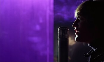 Movie still from “Help!” (1965), directed by Richard Lester – A person with a microphone in front of a purple background; Close Up shot, Low angle