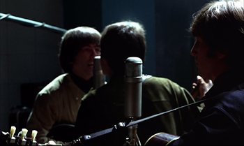 Movie still from “Help!” (1965), directed by Richard Lester – A group of people that are sitting around a microphone; Close Up shot, Over the shoulder angle