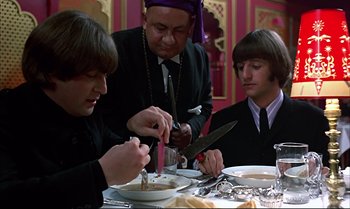 Movie still from “Help!” (1965), directed by Richard Lester – A group of people sitting at a table with food; Close Up shot, High angle