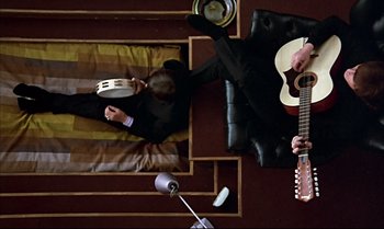 Movie still from “Help!” (1965), directed by Richard Lester – Two men in suits are playing music on a guitar; Wide shot, Overhead angle