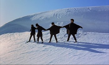 Movie still from “Help!” (1965), directed by Richard Lester – A group of people standing on top of a snow covered slope; Extreme Wide shot, Overhead angle