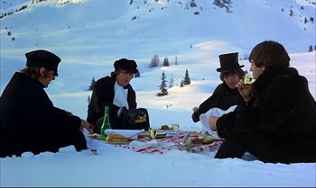 Movie still from “Help!” (1965), directed by Richard Lester – A group of people sitting on a blanket in the snow; Wide shot, High angle
