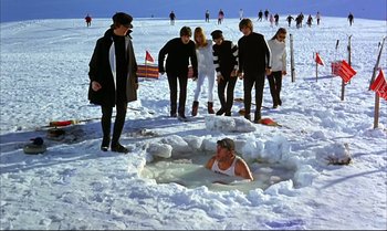 Movie still from “Help!” (1965), directed by Richard Lester – A group of people standing in the snow near a person in a pool of water; Wide shot, High angle