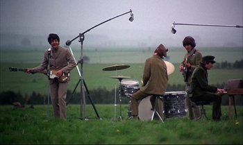 Movie still from “Help!” (1965), directed by Richard Lester – A group of people playing instruments in a field; Extreme Wide shot, High angle