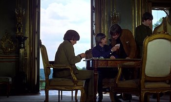 Movie still from “Help!” (1965), directed by Richard Lester – A group of people sitting at a table playing a game; Wide shot, High angle