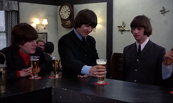 Movie still from “Help!” (1965), directed by Richard Lester – A man in a suit and tie holding a glass of beer at a bar; Medium shot, High angle