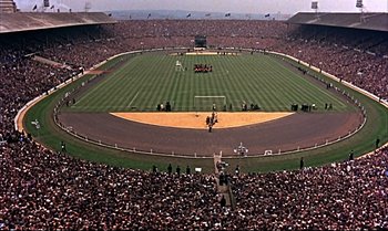 Movie still from “Help!” (1965), directed by Richard Lester – A large crowd of people watching a baseball game in a stadium; Extreme Wide shot, High angle