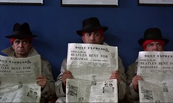 Movie still from “Help!” (1965), directed by Richard Lester – A group of men sitting next to each other holding newspapers; Medium shot, High angle