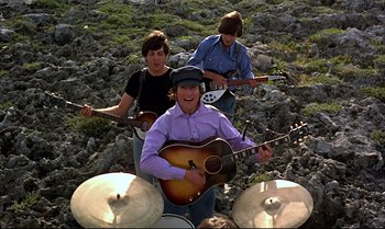 Movie still from “Help!” (1965), directed by Richard Lester – A group of young people playing instruments in a field; Wide shot, Low angle